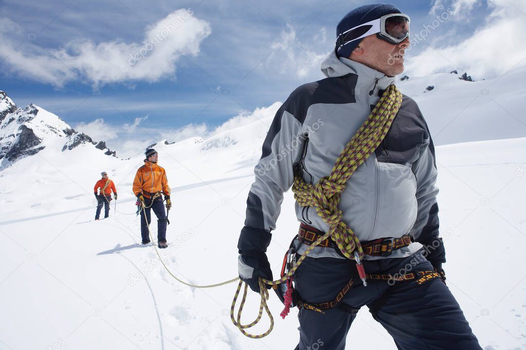 Three hikers joined by safety line in snowy mountains