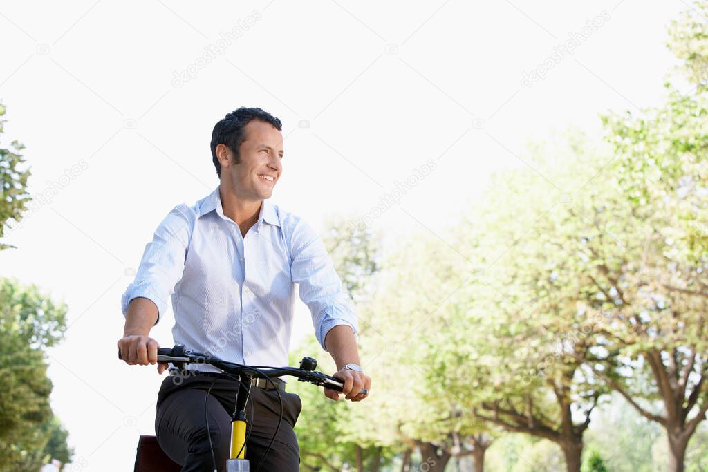 Businessman riding bicycle in park low angle
