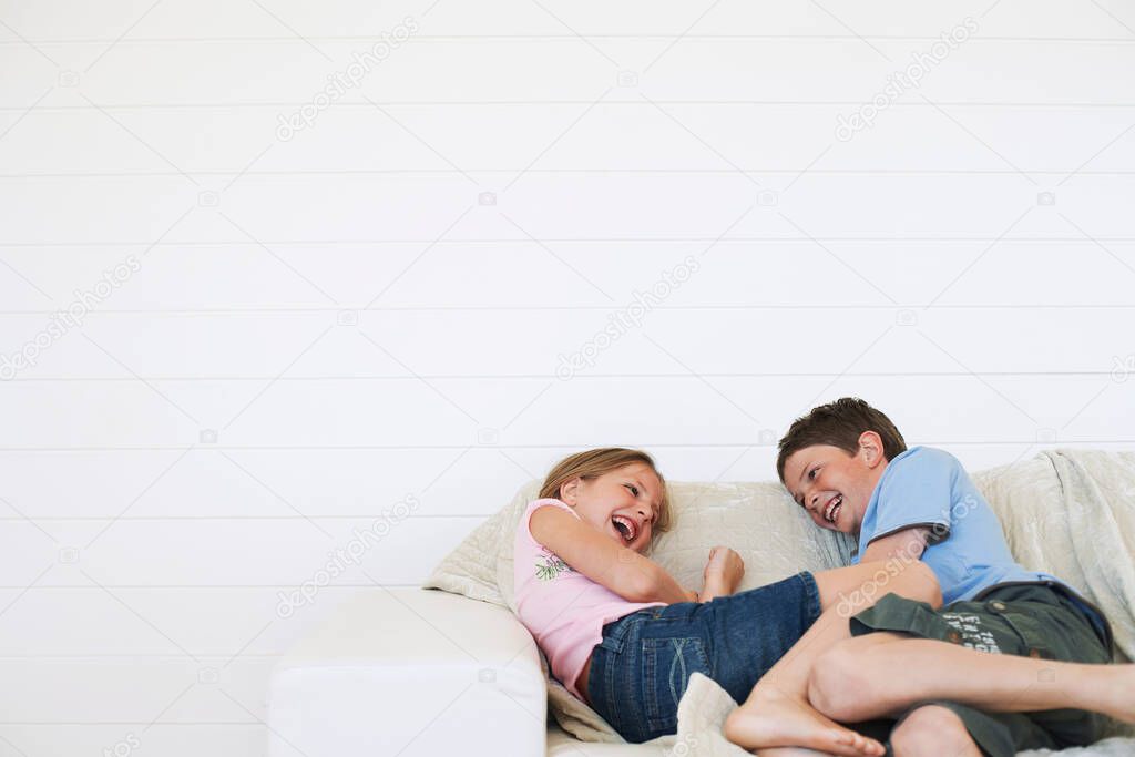 Young boy and girl laughing on couch in weather boarded room