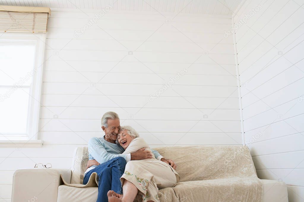 Senior couple embracing sitting on couch in living room