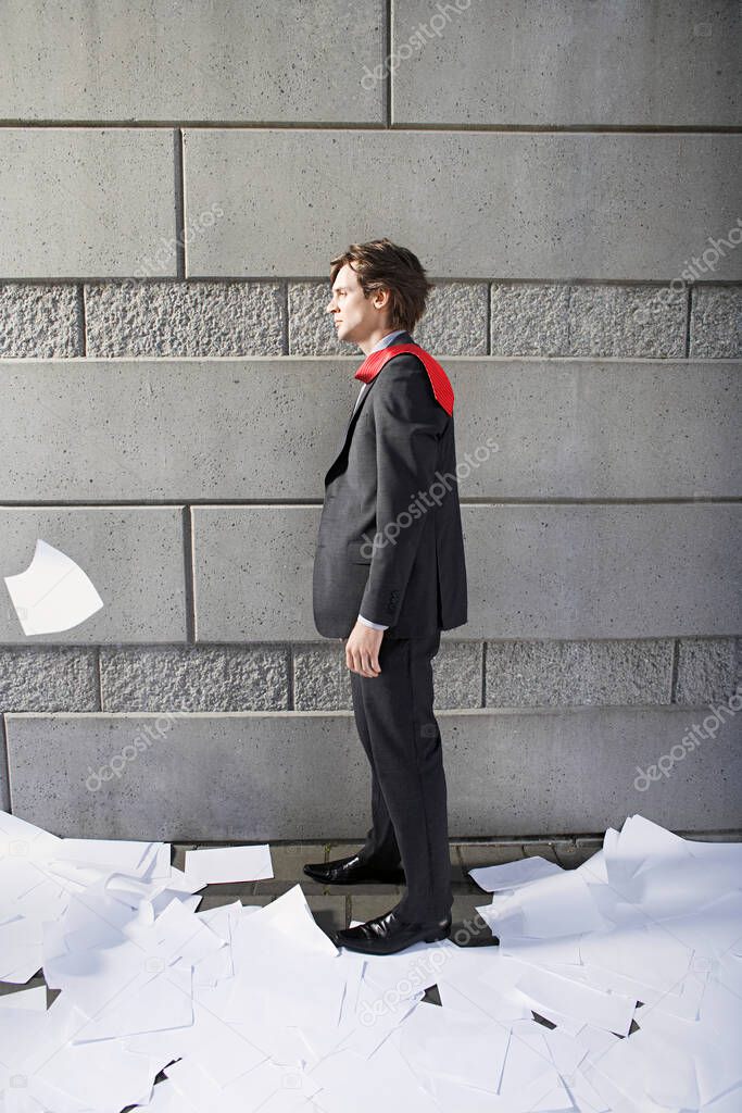 Business man surrounded by paper material beside wall
