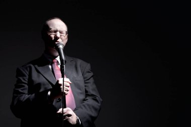 Takım elbiseli adam mikrofona şarkı söylüyor.