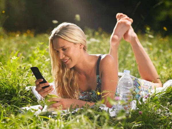 携帯電話を使って草原に寝そべっている若い女性 — ストック写真