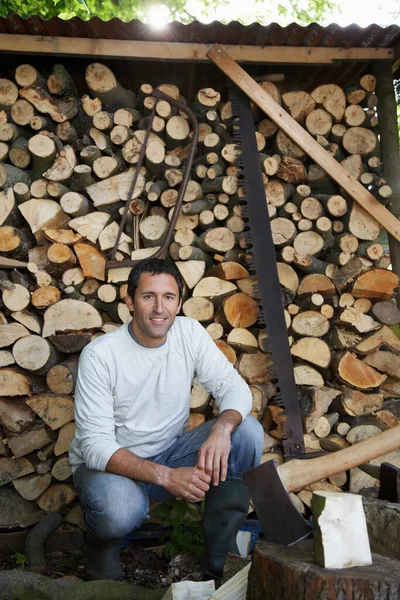 Man crouching beside axe at timber shed portrait