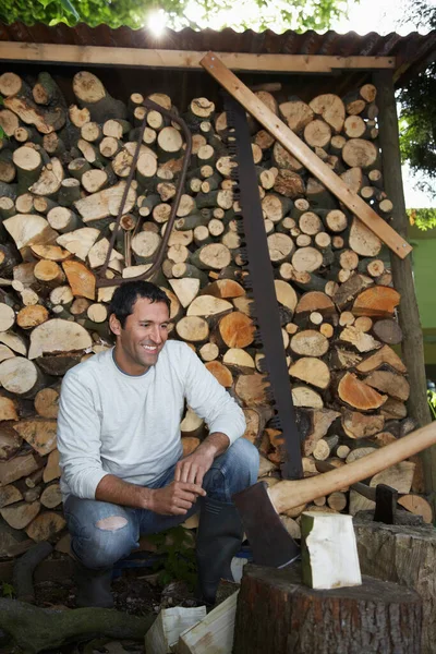 Man Hurkend Naast Bijl Bij Houtschuurtje — Stockfoto