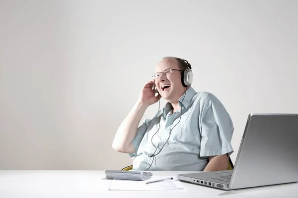 Businessman with earphones laughing at desk