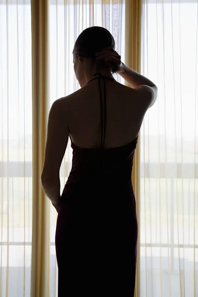 Young woman standing by window back view