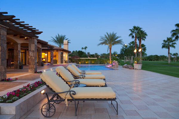 шезлонги в патио у бассейна возле роскошного поместья