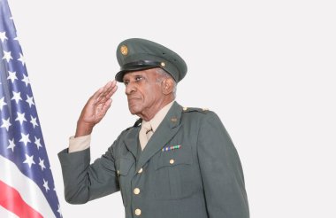 Üst düzey erkek ABD askeri subayı gri arka planda Amerikan bayrağını selamlıyor