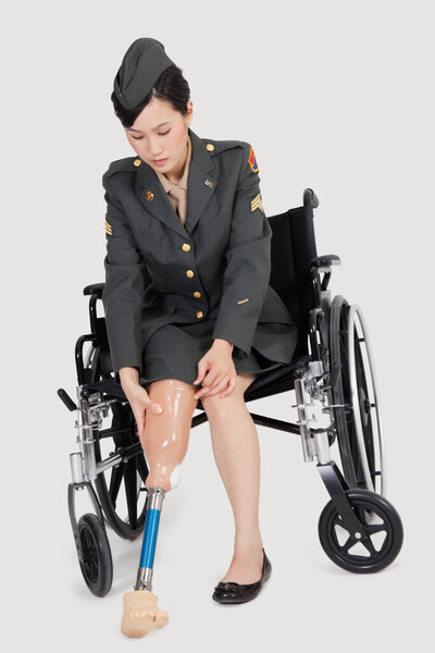 Female US military officer in wheelchair fitting prosthesis foot over gray backgrounds