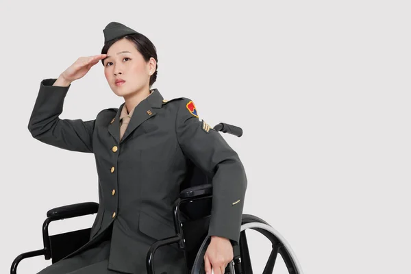 Perempuan Perwira Militer Kursi Roda Hormat Atas Latar Belakang Abu — Stok Foto