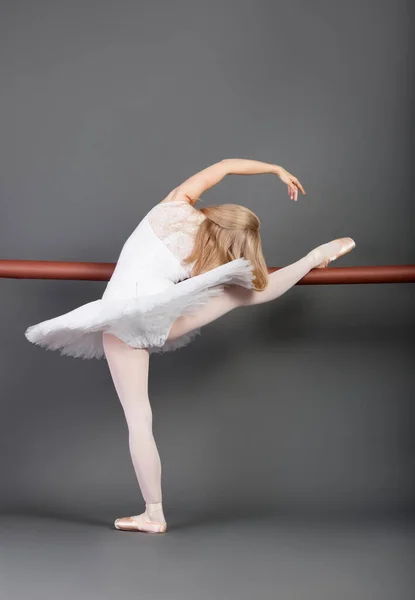 年轻的芭蕾舞女舞者在灰色背景下伸展在芭蕾舞吧 — 图库照片