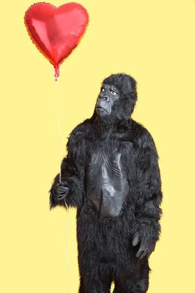身穿大猩猩服装的年轻人站在黄色的背景上看着心形气球 — 图库照片