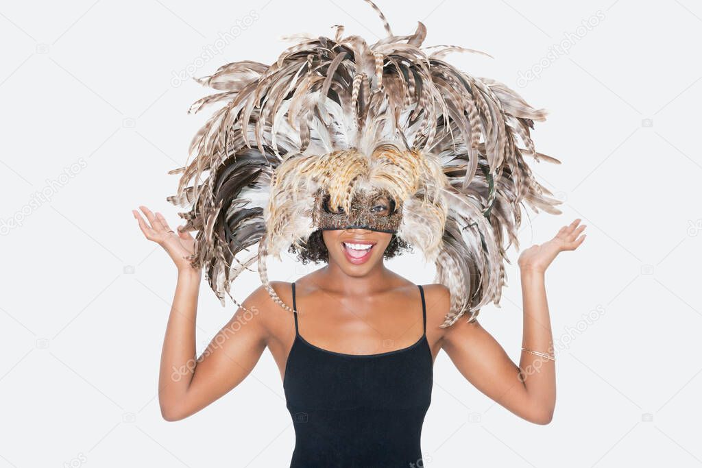 Portrait of happy African American woman wearing a feather mask over gray background