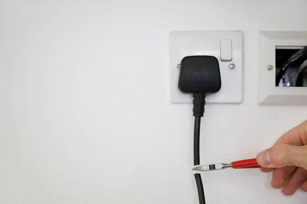 Cropped Shot Hand Cutting Electrical Cord Attached Outlet White Wall — Stock Photo, Image