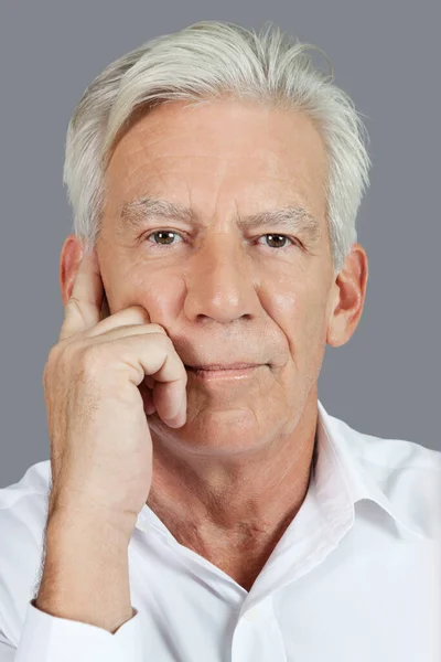 Close-up portrait of senior man thinking over gray background