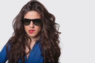 Gri arkaplanı ısırırken güneş gözlüğü takan şehvetli genç bir kadının portresi.