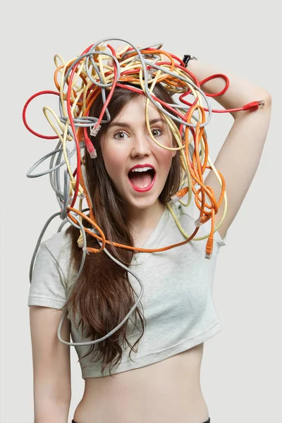 Portrait Shocked Young Woman Head Tangled Colorful Cables Gray Background — Stock Photo, Image