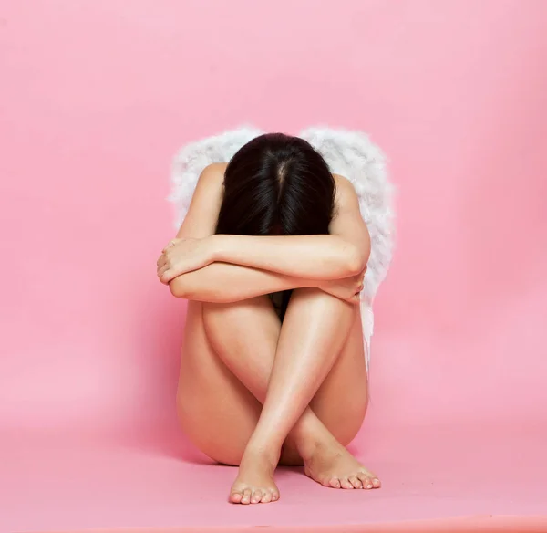 忧郁的亚洲女人 长着天使般的翅膀 靠着粉红的背景坐在地板上 — 图库照片