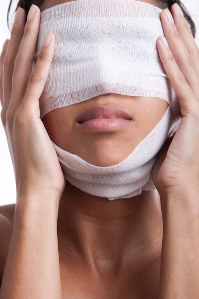 Young woman with head wrapped in bandage against white background