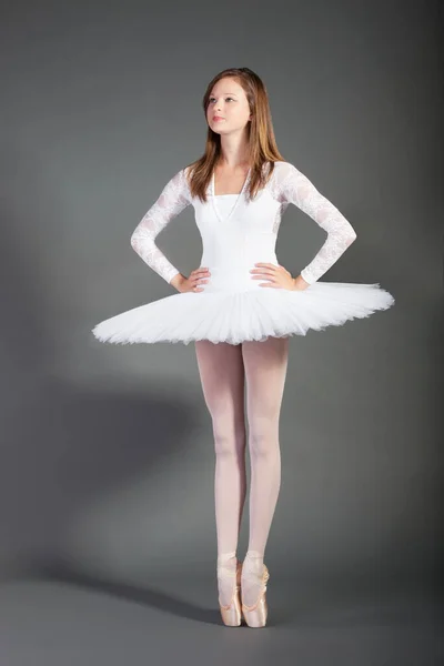 Young female ballet dancer tiptoeing against grey background