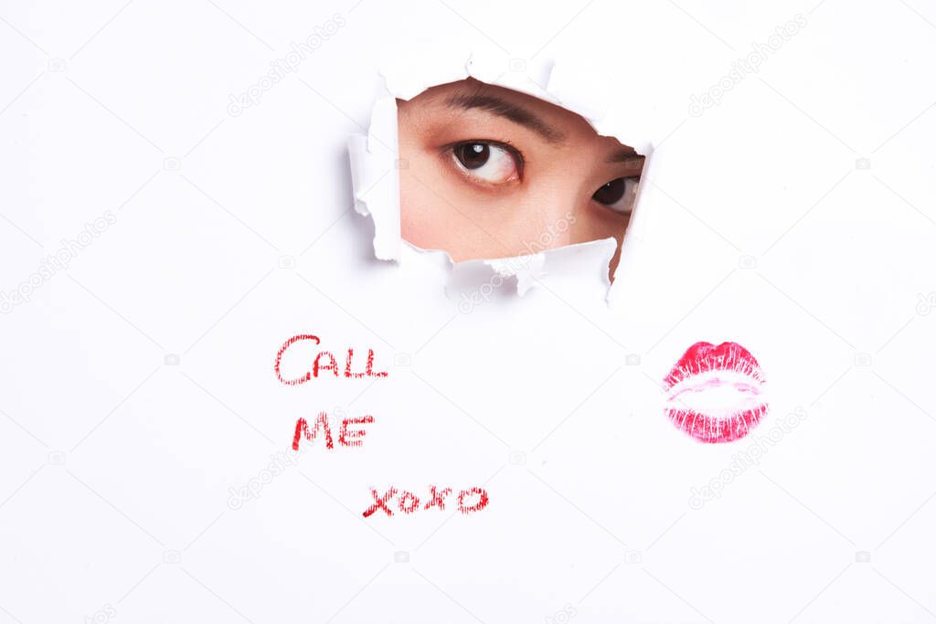 Young woman peeking through ripped paper with text message and lipstick mark