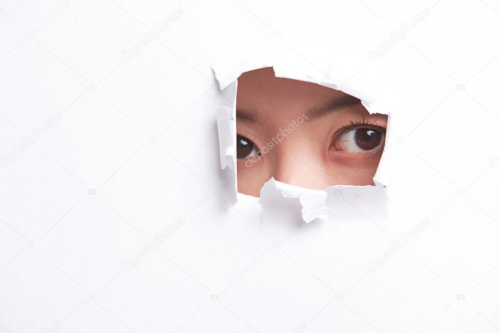 Portrait of young woman peeking through a ripped paper hole