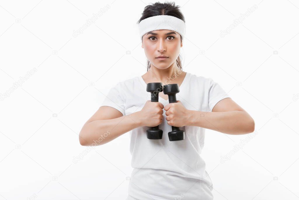 Portrait of young Asian sportswoman raising dumbbell over white background