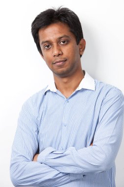 Kollarını kavuşturup beyaz arka planda duran kendine güvenen genç Hintli bir adamın portresi.