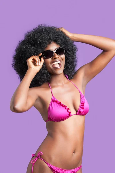 幸せな若いです女性の肖像でサングラスとビキニPositing上の紫の背景 — ストック写真