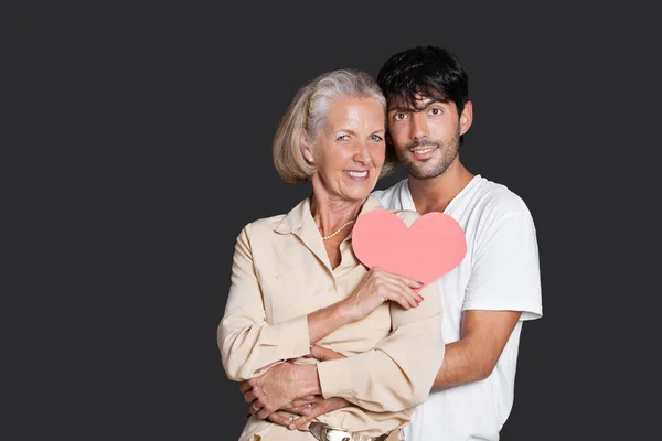 Young Man Embracing Senior Woman Holding Red Paper Heart Black — Stock Photo, Image