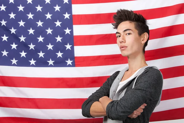 自信に満ちた若者の肖像画アメリカ国旗に向かって腕を組んで立っている — ストック写真