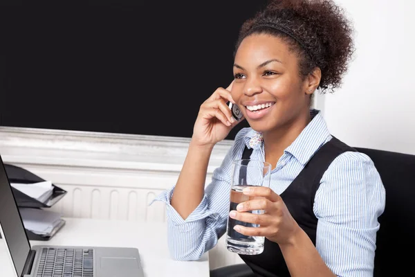 オフィスのデスクでノートパソコンの前で携帯電話を使用して幸せなビジネス女性 — ストック写真
