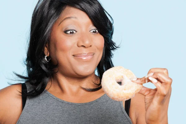 体重超标的混血儿女人在蓝色背景下吃甜甜圈 — 图库照片