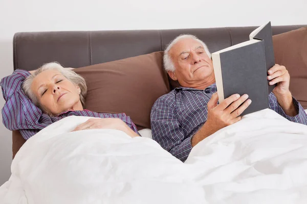 Elderly Man Reading Book While Spouse Sleeping Bedroom — Stock Photo, Image