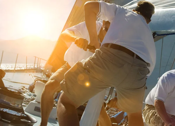 Two sailing crew members working rigging on sail boat with lens fare