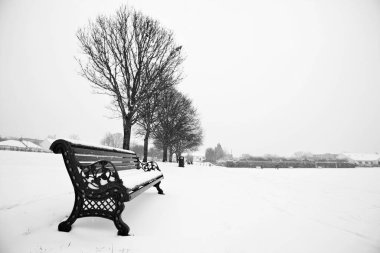 Park bankı ve park karla kaplı.