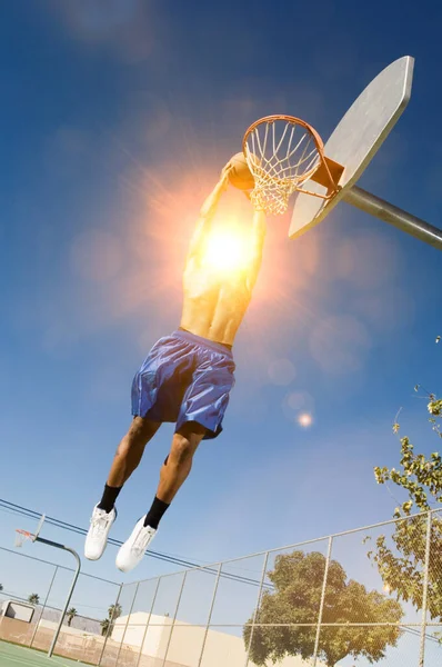 Man about to slam dunk ball on basketball court with strong sun shining lensflare