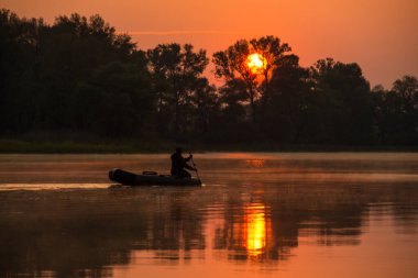 Bir adam kırmızı bir günbatımında gölde şişme bir teknede yüzüyor.