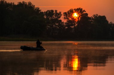 Bir adam kırmızı bir günbatımında gölde şişme bir teknede yüzüyor.