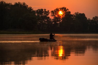 Bir adam kırmızı bir günbatımında gölde şişme bir teknede yüzüyor.