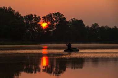 Bir adam kırmızı bir günbatımında gölde şişme bir teknede yüzüyor.