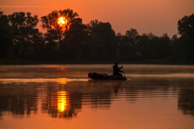 Bir adam kırmızı bir günbatımında gölde şişme bir teknede yüzüyor.