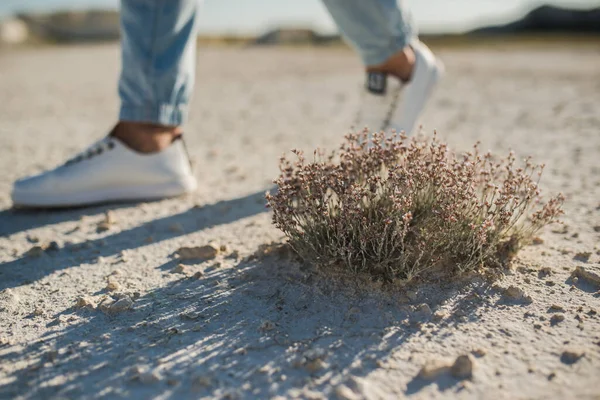 the feet of a girl in white sneakers are walking in a desert area
