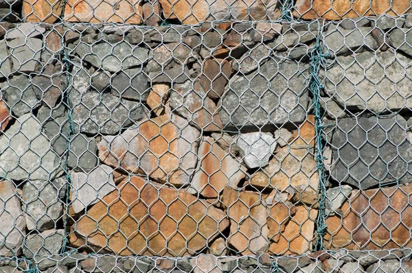 Wall of several gabions. The mesh cells of the cubic form are filled with mountain stones of various shapes