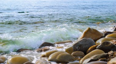 Taşlı sahilde yuvarlanan deniz dalgaları, yakın bir yerde