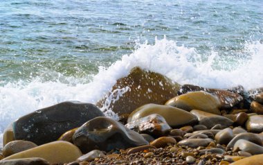 Taşlı sahilde yuvarlanan deniz dalgaları, yakın bir yerde