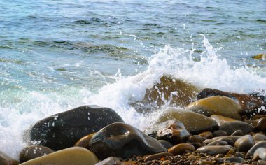 Taşlı sahilde yuvarlanan deniz dalgaları, yakın bir yerde