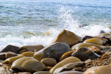 Taşlı sahilde yuvarlanan deniz dalgaları, yakın bir yerde
