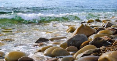 Taşlı sahilde yuvarlanan deniz dalgaları, yakın bir yerde